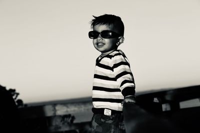 Boy wearing sunglasses while standing by railing against sky