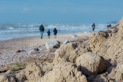 Rocks, stones and sand fall from a cliff on the beach with people walking. erosion concept