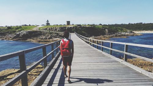 Woman standing on footbridge by sea against clear sky