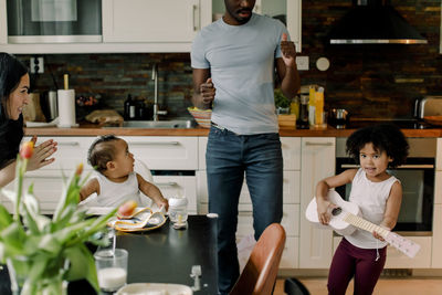 Girl playing guitar by family in kitchen at home