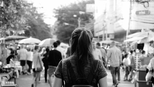 Rear view of woman walking towards crowd on street