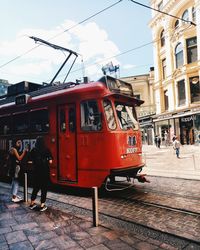 People on railroad track in city against sky