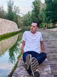 Portrait of young man sitting on rock by lake