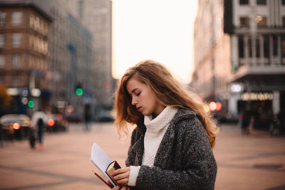 Young woman using phone while standing on street in city