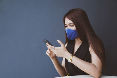 Young woman using mobile phone while standing on wall