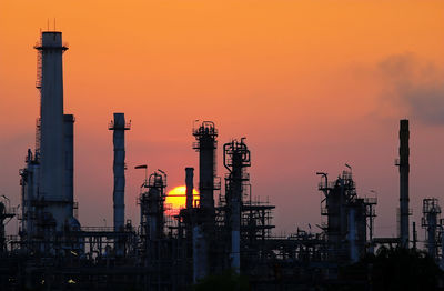 Silhouette factory against sky during sunset