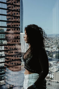 Side view of young woman standing against cityscape