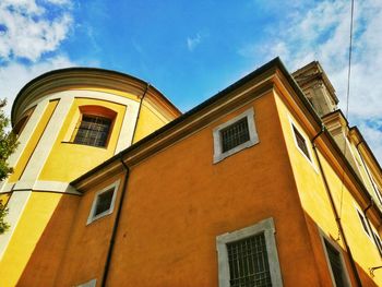 Low angle view of yellow building against cloudy sky