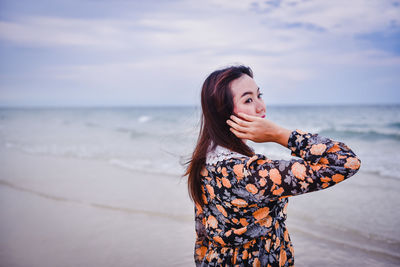 Young woman standing at beach against sky