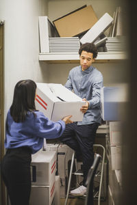 Salesman giving appliance to saleswoman while standing on ladder in store