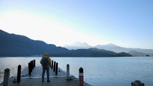 Rear view of man standing on pier over lake against clear sky