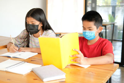 Asian girl boy student wearing face mask studying writing notes doing homework in library. learning