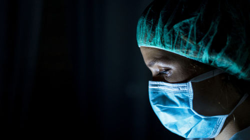 Portrait of young female surgeon, wearing mask and a surgical mask, in front of black background