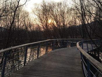 Footbridge over river against sky during sunset