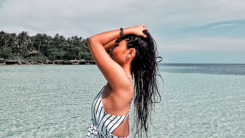 Young woman in bikini standing on beach against sky