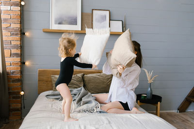 Active mother and daughter holding pillows fighting on bed