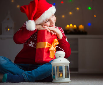 Full length of boy wearing santa hat holding gift box sitting at home