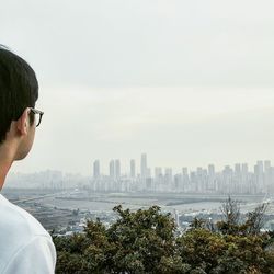 Man looking at skyscrapers in city against sky