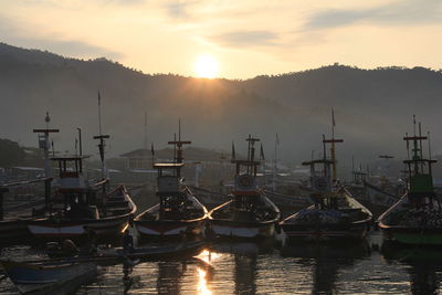 Sailboats moored at harbor against sky during sunset