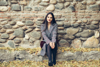 Portrait of woman sitting against stone wall during autumn