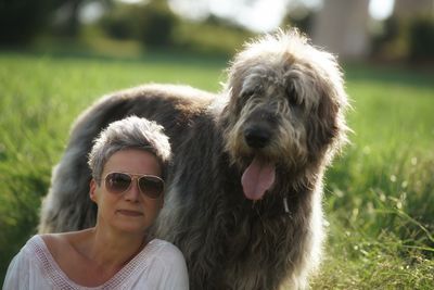 Confident mature woman with hairy dog sitting on grassy field