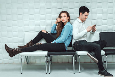 Young couple looking at camera while sitting on wall