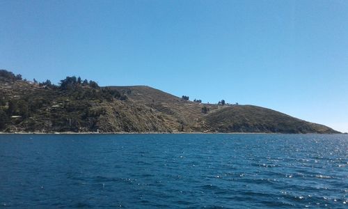 Scenic view of sea and mountains against clear blue sky