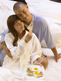 Smiling mid adult couple with food on bed at home