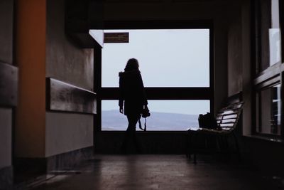 Rear view of silhouette woman standing at window