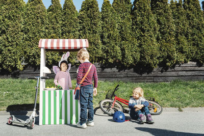 Boy standing at food stall while friend imitating as seller on footpath