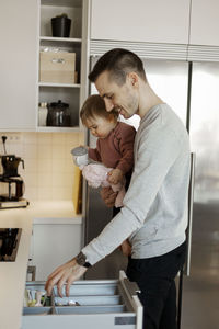 Father carrying toddler girl in kitchen