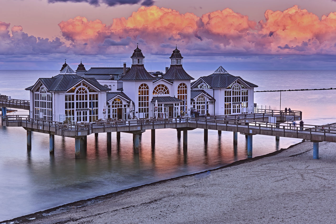 PIER OVER SEA AGAINST BUILDINGS AT SUNSET