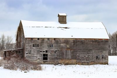 Abandoned barn on snow covered field against sky
