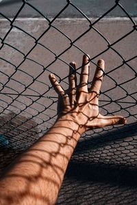 Hand with shadow shapes grabbing a metallic fence