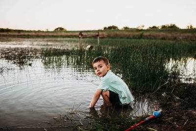 Young boy sitting in lake trying to catch fish
