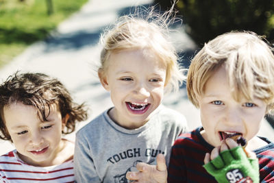 Portrait of happy boy eating ice cream while walking with friends at yard