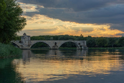 Arch bridge over river against sky during sunset