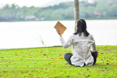 Rear view of woman holding book sitting at park