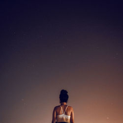 Rear view of woman sitting against sky at night