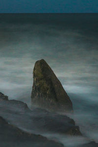 Rock formations in sea against sky at dusk