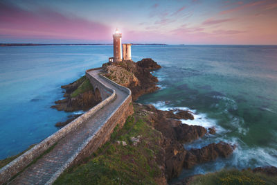 Lighthouse by sea against sky during sunset