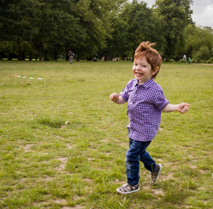Cute boy running on grass against trees