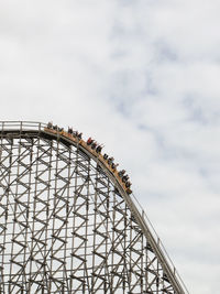 Low angle view of people on rollercoaster against cloudy sky