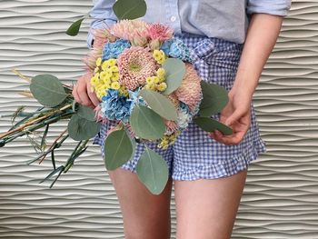 Midsection of woman holding bouquet against wall