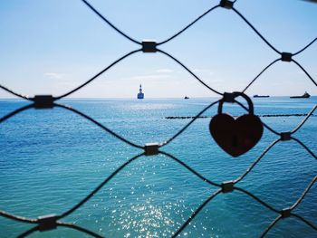 Close-up of chainlink fence by sea against sky