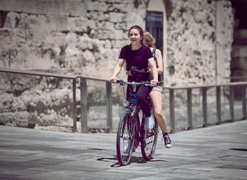 Full length of young woman riding bicycle on city