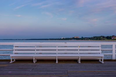 Empty bench by sea against sky