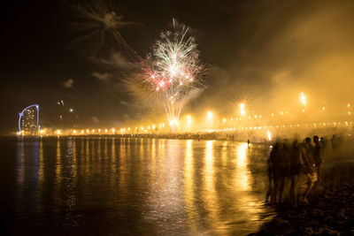 Group of people at beach enjoying firework display at night