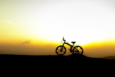 Silhouette bicycle on field against sky during sunset