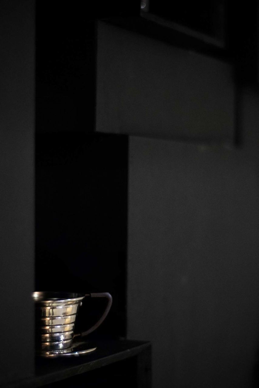 CLOSE-UP OF COFFEE CUP ON TABLE AGAINST ILLUMINATED WALL